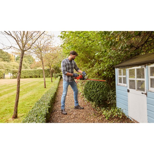 BLACKDECKER BEHTS401 hedge trimmer used on garden bushes near a blue shed, outdoor setting.