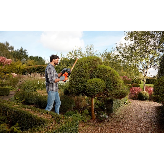 BLACKDECKER BEHTS401 hedge trimmer in use trimming shaped bushes in a garden.