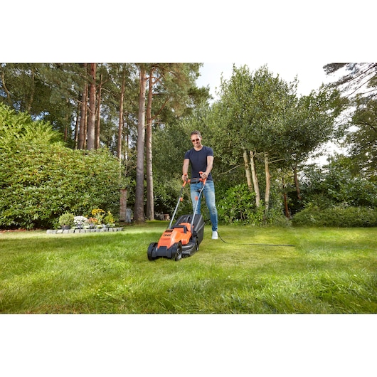 BLACKDECKER BEMW451BH electric lawn mower in use outdoors on grass lawn, garden setting.