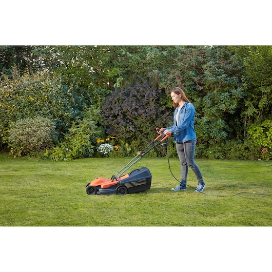BLACKDECKER BEMW451BH lawn mower with grass bag in use on a green lawn, user walking behind.