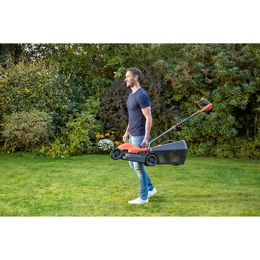 BLACKDECKER BEMW451BH lawn mower in use, carried by a person on a green garden lawn.