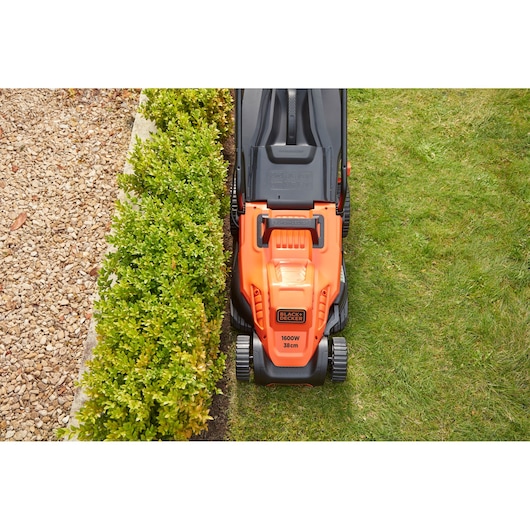 Photo of BLACKDECKER BEMW471BH orange lawn mower cutting grass next to green hedge and gravel path.