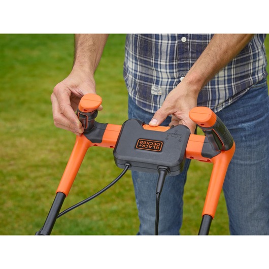 BLACKDECKER BEMW471BH lawn mower handle controls close-up, orange and black details, outdoor use.
