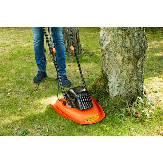 BLACK+DECKER BEMWH551 orange and black electric hover mower cutting grass around a tree.