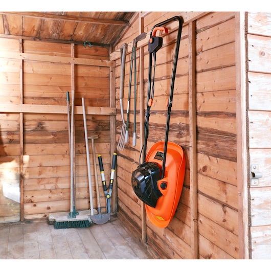 BLACKDECKER BEMWH551 lawn mower hanging on wooden shed wall with garden tools nearby.