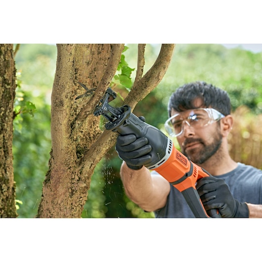 BLACKDECKER BES301K reciprocating saw cutting tree branch outdoors with gloved hands.