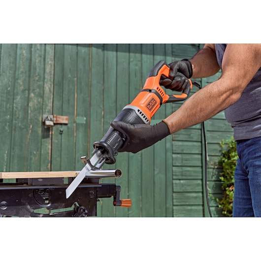 BLACKDECKER BES301K reciprocating saw cutting metal pipe outdoors, close-up with gloved hands.