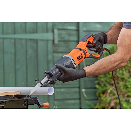 Photo of BLACKDECKER BES301K reciprocating saw cutting a white PVC pipe outdoors.