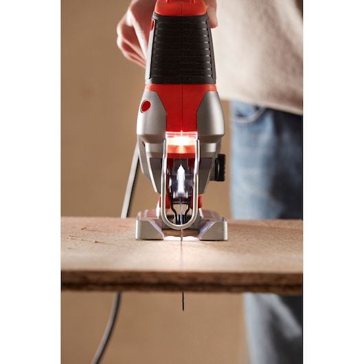 BLACKDECKER BES610 jigsaw front view cutting wood plank, red and black body.