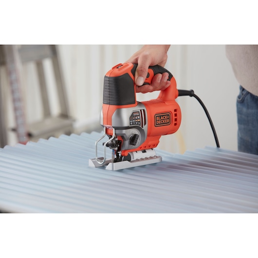 Photo of BLACKDECKER BES610 jigsaw cutting corrugated sheet, orange and black design, handheld power tool.