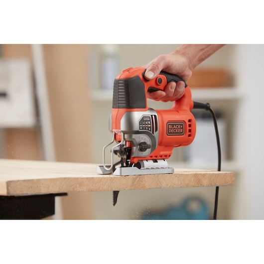BLACKDECKER BES610 jigsaw cutting wood, close-up of orange and black tool held by hand.
