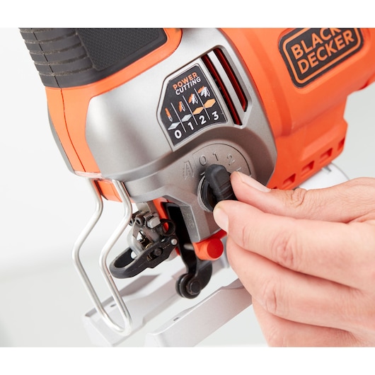 Photo of BLACKDECKER BES610 jigsaw close-up with hand adjusting speed dial, orange and silver body.