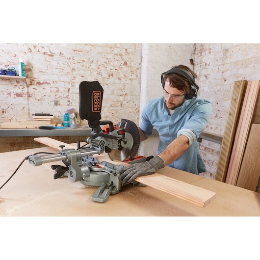 BLACK+DECKER BES700 miter saw in use cutting wood in a workshop setting, operator wearing safety gear.