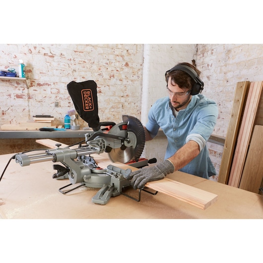 Photo of BLACKDECKER BES710 sliding miter saw cutting wood in workshop, operator wearing safety gear.