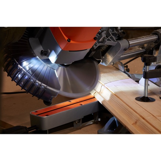 BLACKDECKER BES710 miter saw cutting light wood, close-up angle, showing illuminated blade and cutting action.