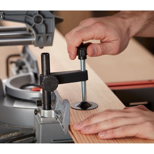 BLACKDECKER BES710 miter saw clamping a wooden board, close-up of adjustment mechanism and hands.