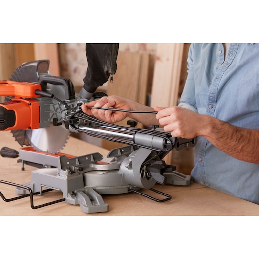 Photo of BLACKDECKER BES710 mitre saw on workbench, person adjusting power cord, close-up side angle.
