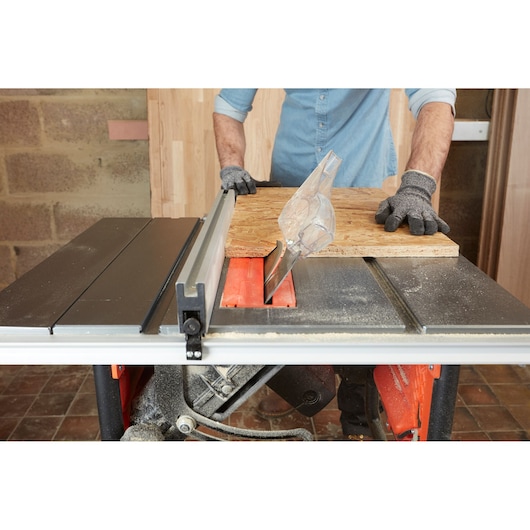 BLACKDECKER BES720 table saw in use cutting wood panel, gloves visible, indoor workshop setting.