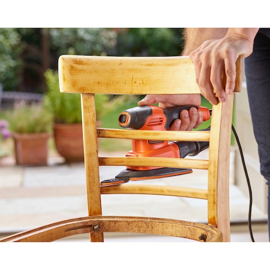 BLACKDECKER BEW200K detail sander used on a wooden chair, close-up view outdoors.