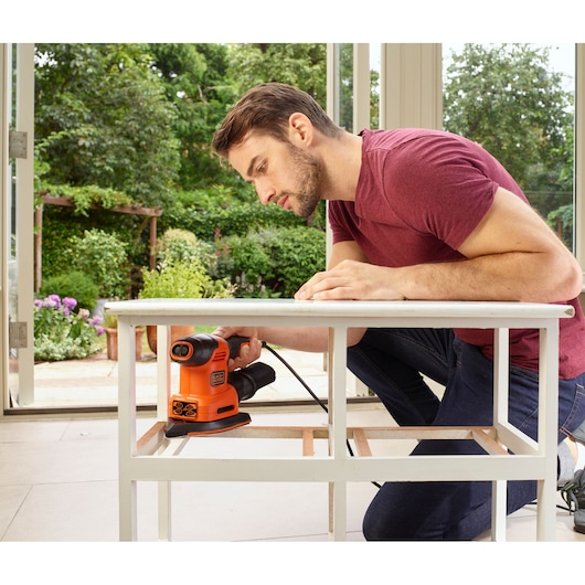 BLACKDECKER BEW200LSA sander used to smooth a white wooden table frame indoors near a window.