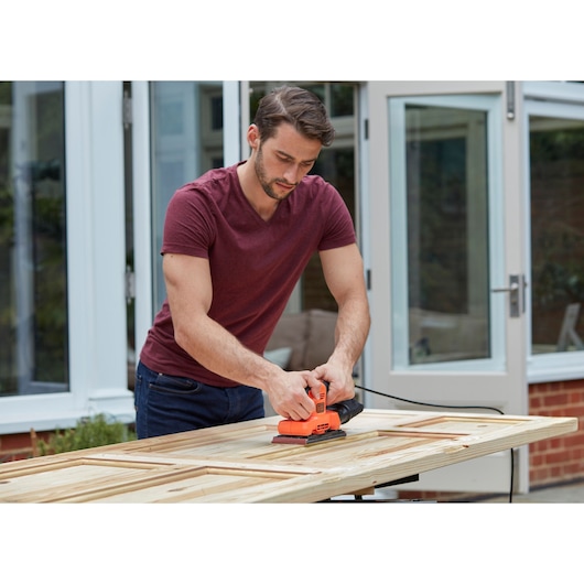 Photo of BLACKDECKER BEW220 sheet sander in use on a wooden door outdoors.