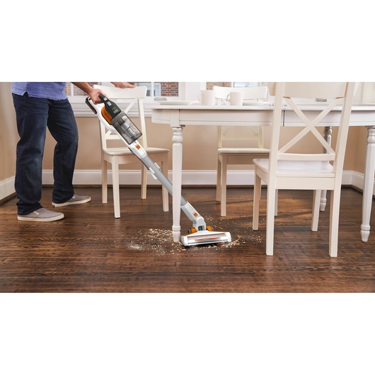 Photo of BLACKDECKER BHFEV1825C cordless stick vacuum cleaning debris on wood floor near dining table.