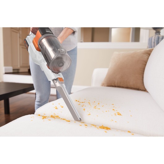 BLACKDECKER BHFEV1825C cordless vacuum cleaning crumbs from a white sofa in a living room.