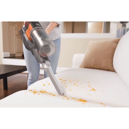 BLACK+DECKER BHFEV182B cordless vacuum cleaning crumbs from a white sofa in a living room.