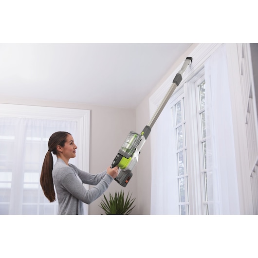 BLACKDECKER BHFEV362DA cordless vacuum cleaner with extension cleaning tool used near a window.