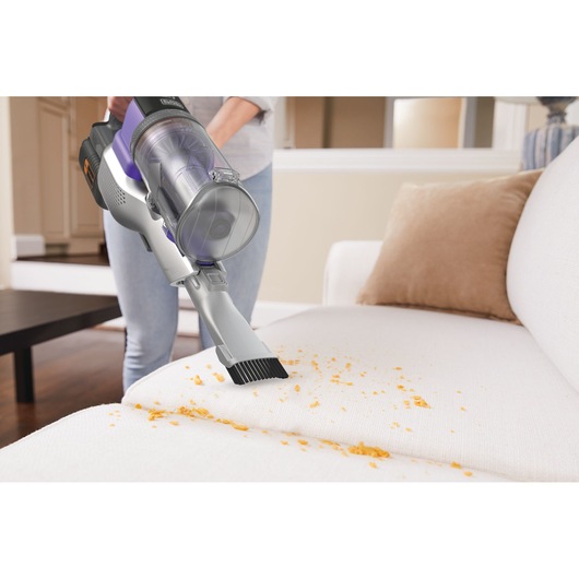 Photo of BLACKDECKER BHFEV362DP cordless vacuum cleaning crumbs from a light-colored sofa in a living room.