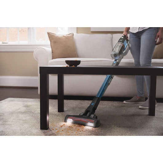 BLACKDECKER BHFEV362D cordless stick vacuum cleaning crumbs under coffee table in living room.