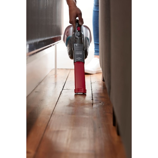 BLACKDECKER BHHV315J handheld vacuum cleaning narrow space beside furniture on wooden floor.