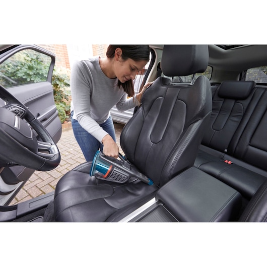 BLACKDECKER BHHV320B handheld vacuum cleaning black leather car seat, indoor usage photography.