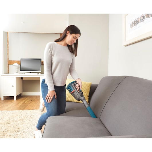 BLACKDECKER BHHV320B handheld vacuum cleaner used to clean grey sofa in living room.