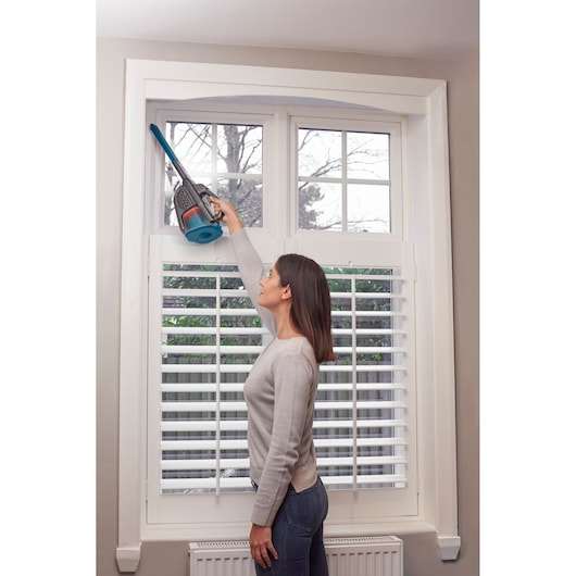 Photo of BLACKDECKER handheld vacuum BHHV320B with extension cleaning a window frame indoors.