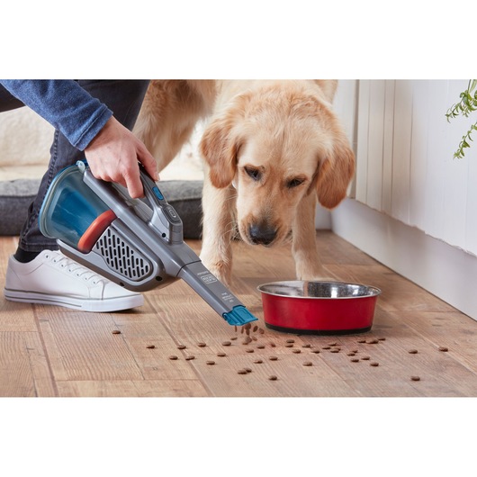 BLACK+DECKER BHHV320B handheld vacuum cleaning pet food near red bowl on wooden floor.