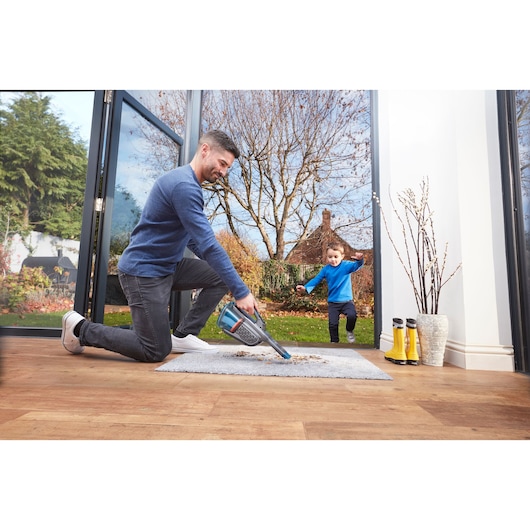 BLACKDECKER BHHV320B handheld vacuum cleaning carpet indoors near open doors, child outside in garden.