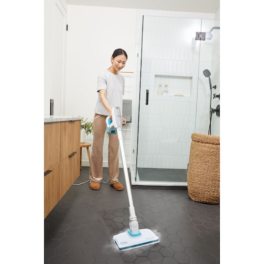 Person using BLACK+DECKER BHSM15FX08 steam mop on hexagonal tile bathroom floor near shower.