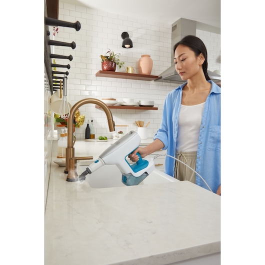 BLACKDECKER BHSM15FX08 steam cleaner used on a kitchen countertop, handheld and emitting steam.