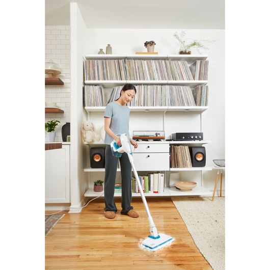 Photo of person using BLACKDECKER BHSM15FX08 steam mop on hardwood floor in modern living room.