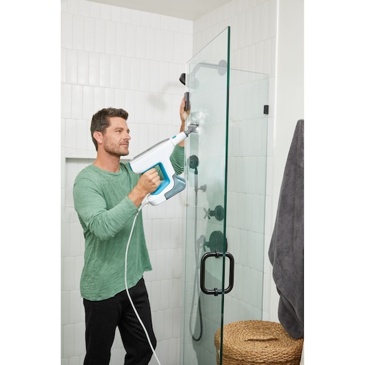 Photo of BLACKDECKER BHSM15FX08 steam cleaner being used on glass shower door in tiled bathroom.