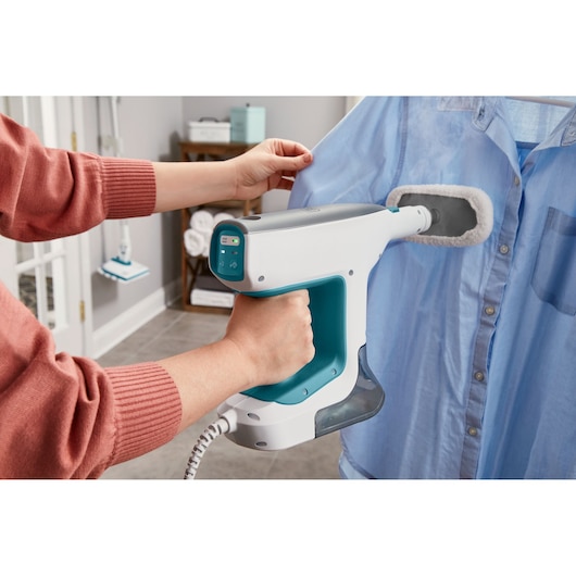 BLACKDECKER BHSM15FX10 handheld steamer used on a blue shirt, close-up angle.