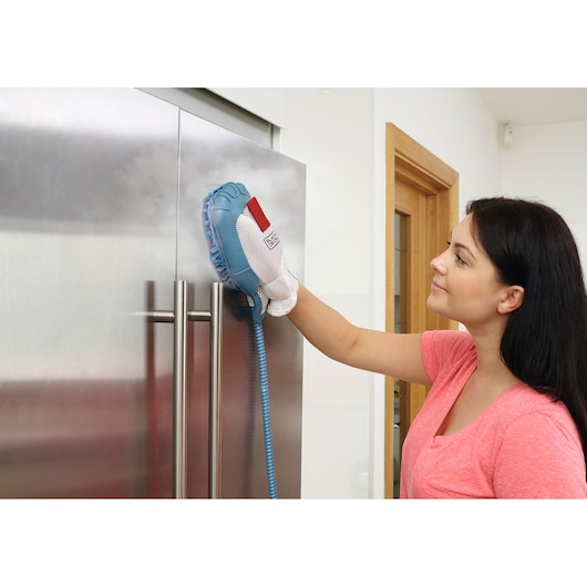 Person using BLACK+DECKER BHSM1615DSM steam cleaning glove on stainless steel refrigerator door.