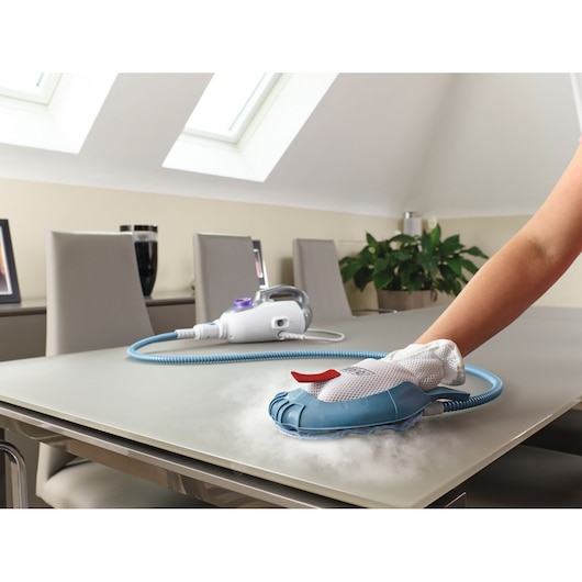 BLACKDECKER BHSM1615DSM handheld steam cleaner cleaning tabletop, close-up, white and blue device with mesh glove.