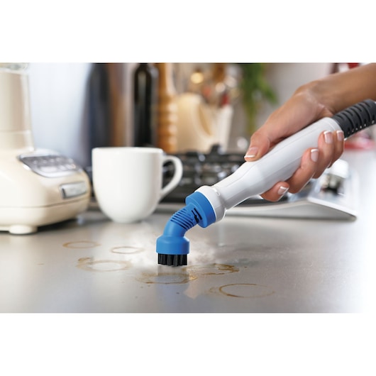 Photo of BLACKDECKER BHSM168D steam cleaner cleaning stained kitchen countertop with blue brush attachment.