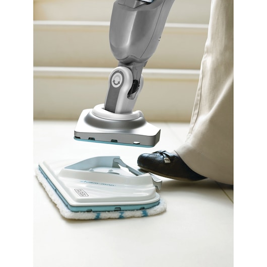 BLACKDECKER BHSM168D steam mop pad attachment being locked into place by a person’s foot on tile floor, side view.