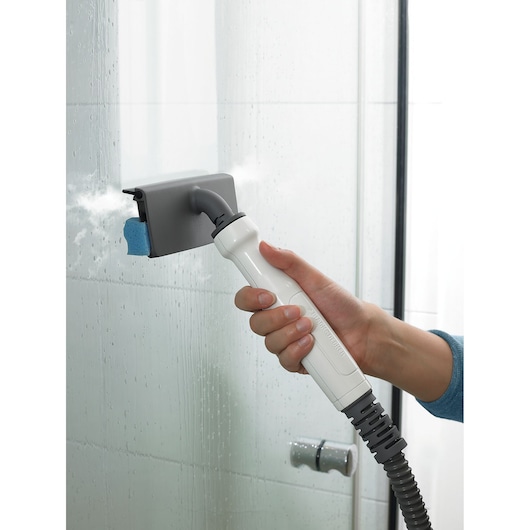 BLACKDECKER BHSM168D steam cleaner used to clean glass shower door with gray rectangular cleaning head, close-up view.