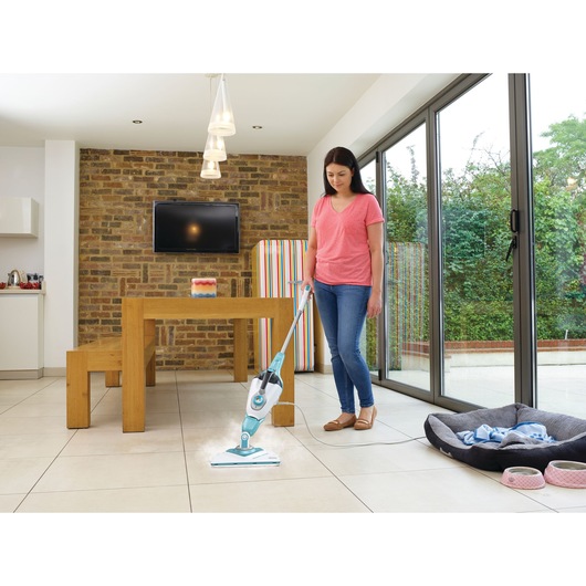 BLACKDECKER BHSM168U steam mop used on tile floor in a modern dining area with wood table and bench.