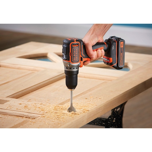Photo of a BLACK+DECKER cordless drill BL186K1B2 in use drilling into a wooden door, visible wood shavings.