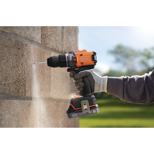BLACK+DECKER BLD683XN cordless hammer drill in use drilling into concrete wall outdoors.